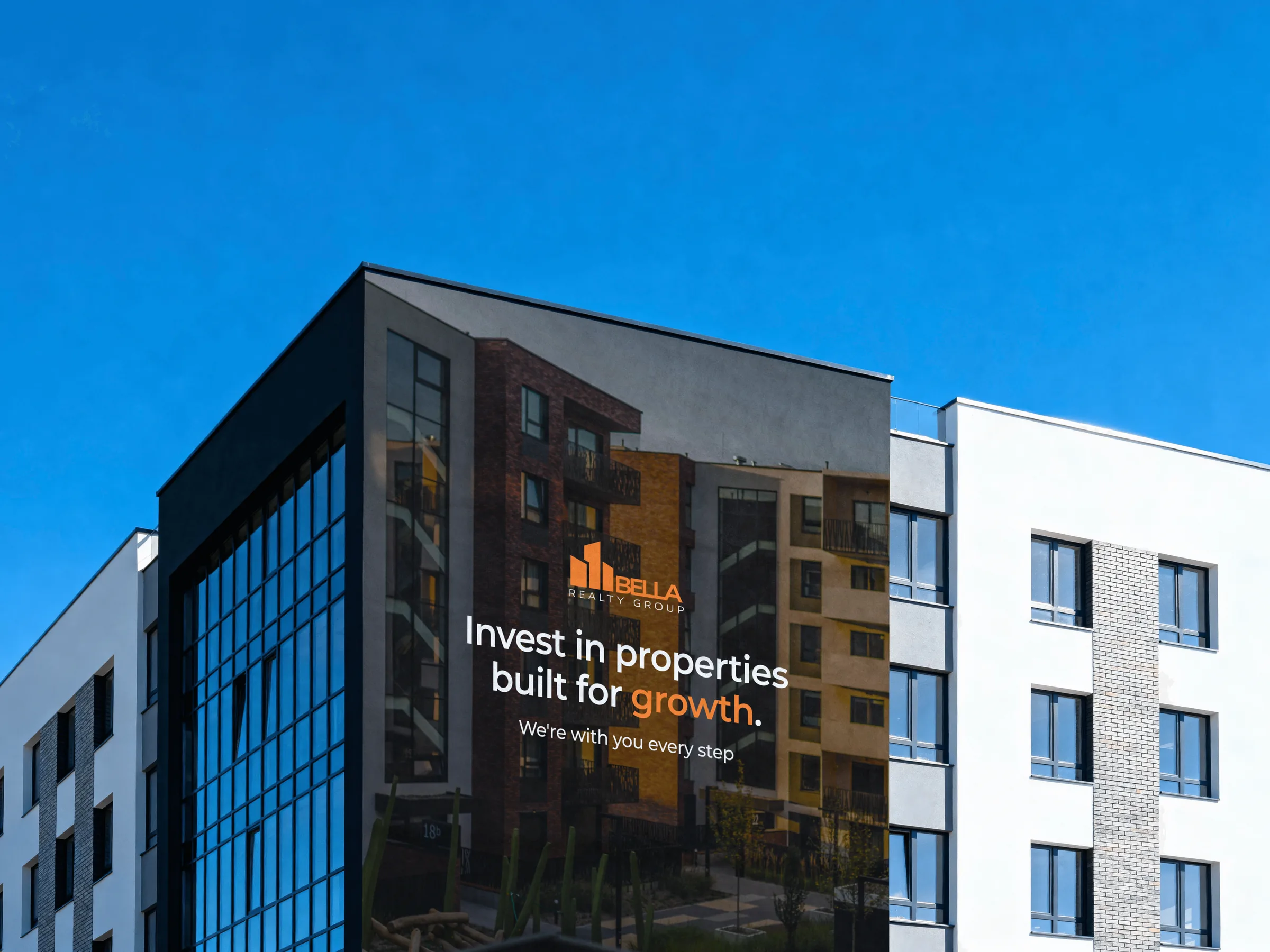A Bella Realty Group ad wrapped around the corner of an apartment building against a blue sky