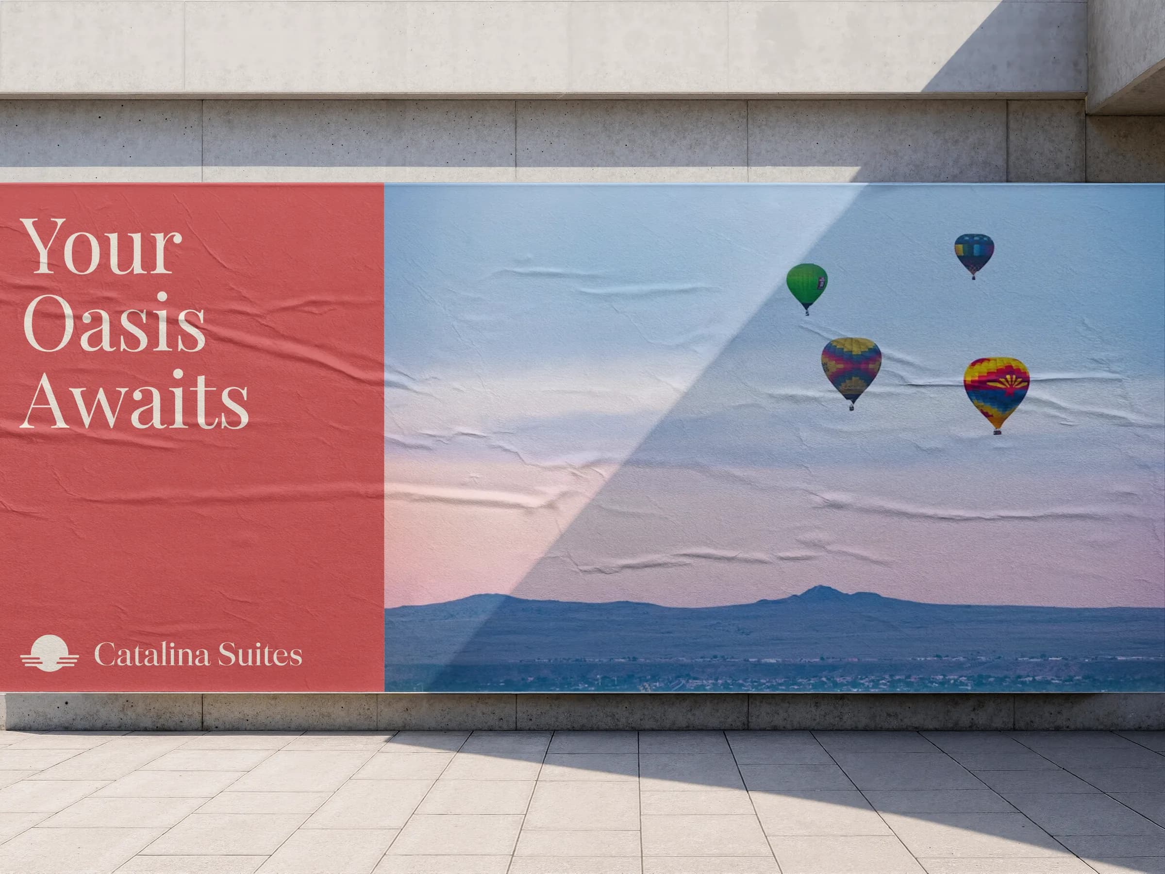 A Catalina Suites billboard reading "Your Oasis Awaits" over hot air balloons above the Albuquerque mountains